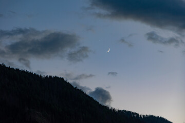Stunning twilight sky with a crescent moon and dark forested mountain slope in the Dolomites, Italy © Franziska Brueckmann