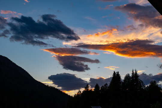 Stunning sunset with glowing golden and dark clouds above a dark forested mountain slope in the Dolomites