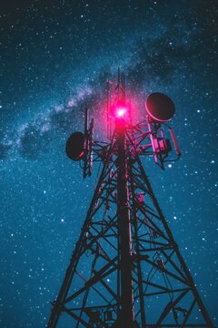 A tall antenna tower stands under the night sky, lit by a red warning light. Stars fill the sky, creating a backdrop of connectivity and technology