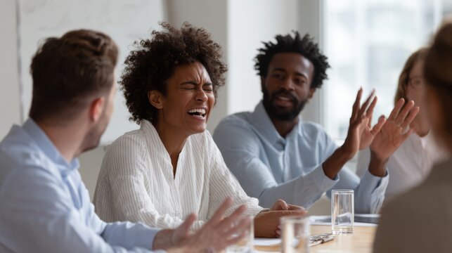A team in a boardroom argues passionately around a conference table. One woman laughs in disbelief while another shows emotional reaction. The scene captures real tension in a corporate setting