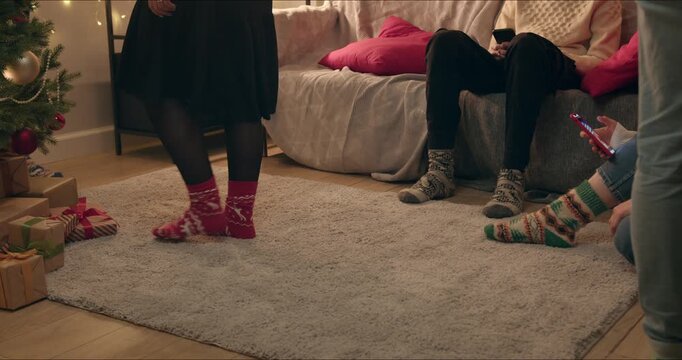  Several pairs of feet in colorful knitted Christmas socks stand and rest together on a plush carpet.
