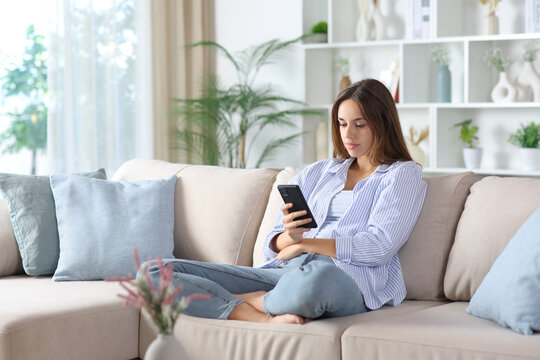 Serious woman in blue is using smart phone on a sofa