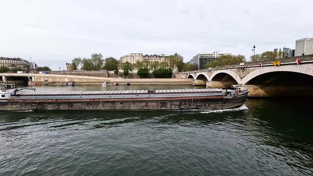 Cargo barge sailing on Seine River under bridge in Paris. Perfect for logistics, transport and travel videos