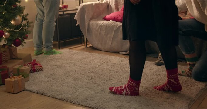 Close-up of friends' feet in red and green patterned Christmas socks resting on a soft carpet at a holiday gathering.
