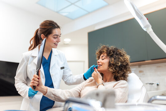 Doctor showing results of facial treatment to patient. Professional cosmetologist using mirror for client. Beauty, skincare and medicine concept. Aesthetic clinic appointment with smiling young woman.