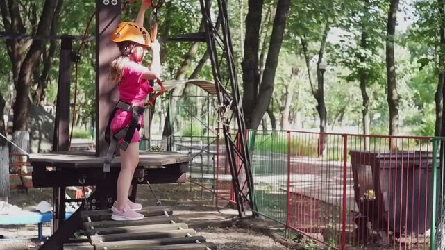 Young girl in a safety helmet and harness ziplining on an adventure course in a summer park
