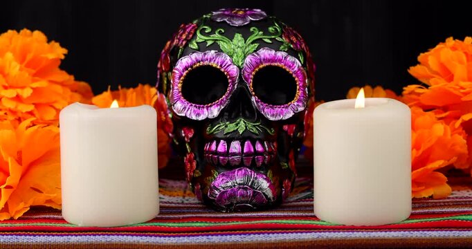 A candle is carefully placed beside a black ornamental skull with vibrant cempasuchil flowers, creating a meaningful Day of the Dead tribute in darkness.