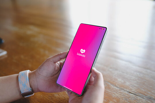 Bangkok, Thailand. July 12, 2026; A close-up view of a person's hands holding a smartphone displaying the Lazada e-commerce shopping app splash screen above a wooden table.