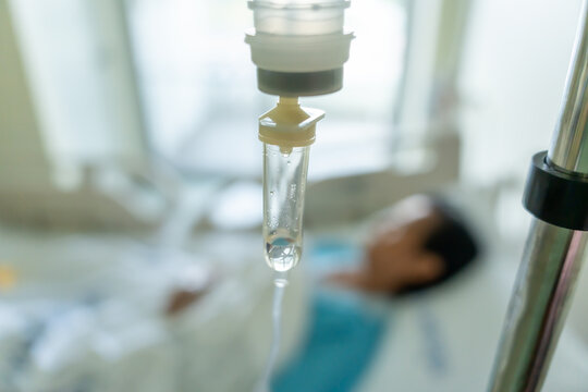 A close-up of a saline bottle strapped to a needle pricked at the hand of a female patient lying in a hospital bed. Medical and treatment of patients concepts