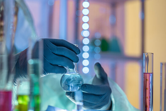 Chemistry laboratory scene with colorful chemical solutions in glass flasks and cylinders, scientist in gloves writing results, analytical experiment workspace.