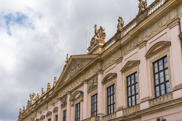 Naklejka premium A low angle view follows the pink facade and sculpted roofline of the Alte Bibliothek. Reliefs, statues and tall windows reveal elaborate historic design.
