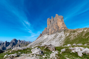 Fototapeta premium Imposing rock towers and green alpine meadows beneath a vast sky near Rifugio Auronzo in the Dolomites