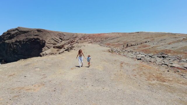 Mother and son running hand in hand along a coastal path in Gran Canaria on a sunny day during their family vacation.