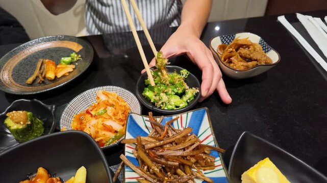 Person Using Chopsticks to Eat Small Asian Side Dishes