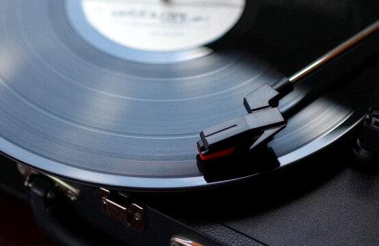 Close up shot of a black vinyl record plate spinning on a retro suitcase turntable with a stylus needle cartridge playing music, selective focus