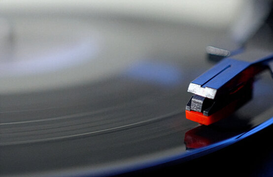 Close up shot of a black vinyl record plate spinning on a retro suitcase turntable with a stylus needle cartridge playing music, selective focus