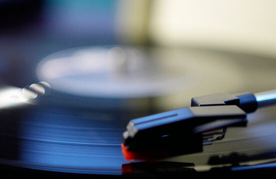 Close up shot of a black vinyl record plate spinning on a retro suitcase turntable with a stylus needle cartridge playing music, selective focus