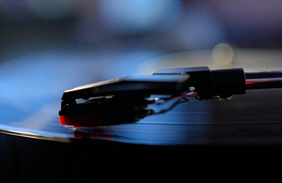 Close up shot of a black vinyl record plate spinning on a retro suitcase turntable with a stylus needle cartridge playing music, selective focus