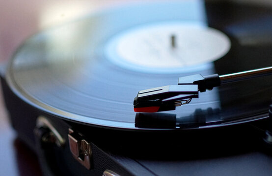 Close up shot of a black vinyl record plate spinning on a retro suitcase turntable with a stylus needle cartridge playing music, selective focus
