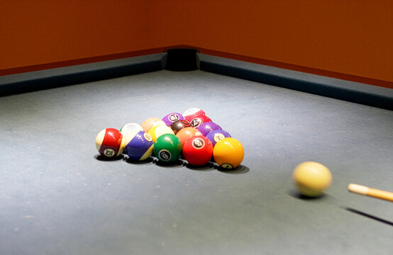 Close up shot of a pool player wearing a black billiard glove, carefully aiming the cue stick at the white cue ball before taking a shot at the colorful numbered balls on a blue felt table.