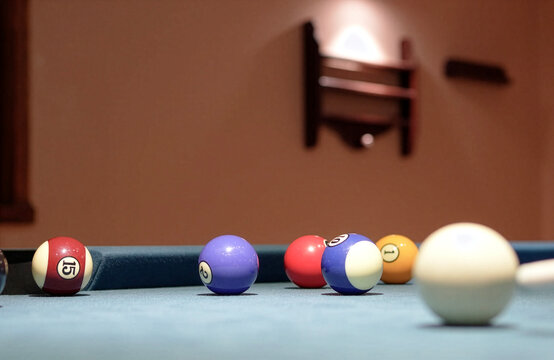Close up shot of a pool player wearing a black billiard glove, carefully aiming the cue stick at the white cue ball before taking a shot at the colorful numbered balls on a blue felt table.