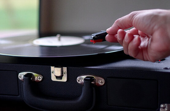 Close up shot of a black vinyl record plate spinning on a retro suitcase turntable with a stylus needle cartridge playing music, selective focus