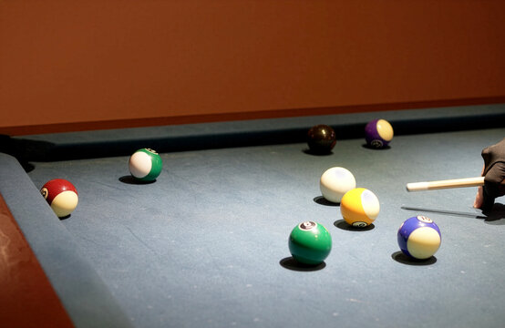 Close up shot of a pool player wearing a black billiard glove, carefully aiming the cue stick at the white cue ball before taking a shot at the colorful numbered balls on a blue felt table.
