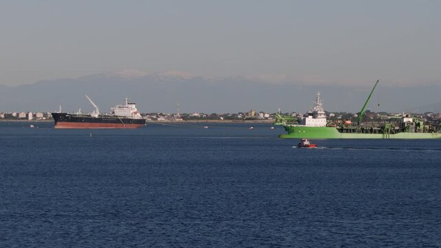 Two large vessels, a cargo tanker and a green dredging ship, anchored in the waters off Thessaloniki's coast.