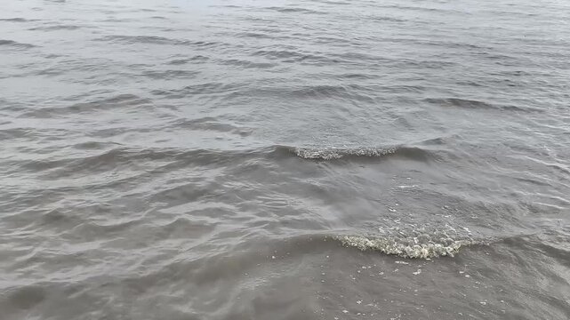 A close-up view of dark ocean waves softly rolling towards the shore with small patches of white foam.