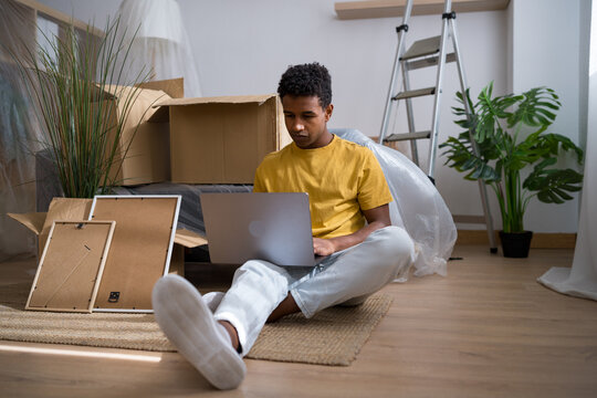 Man using laptop on floor among boxes and plants in new home
