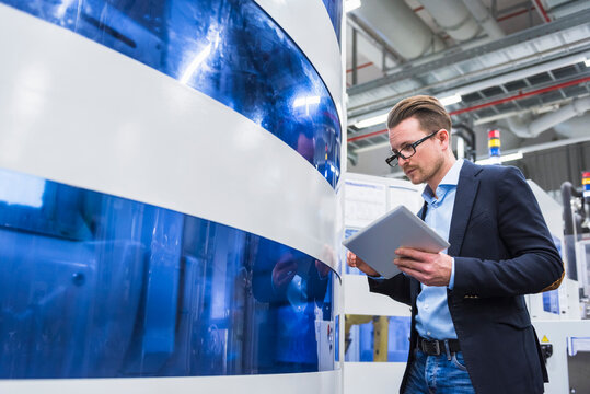 Man holding tablet looking at machine in factory shop floor