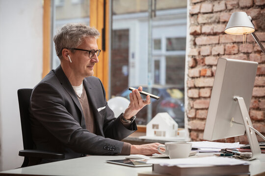 Male professional talking on speaker phone while working on computer in office