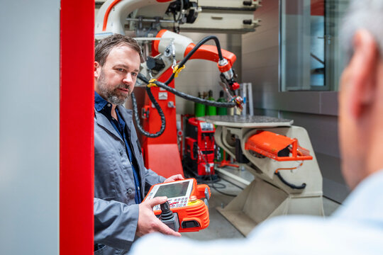 Male engineer operates industrial robot during factory meeting