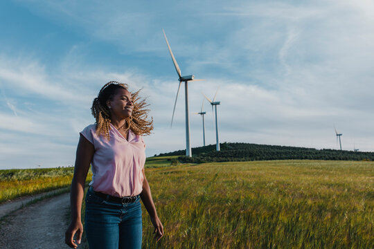 Smiling woman with tousled hair standing in front of wind turbine