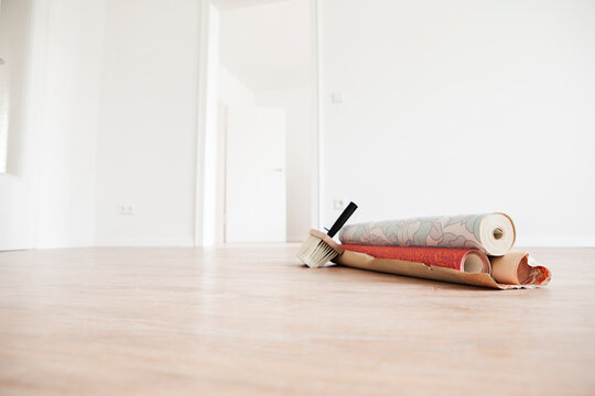 Wallpaper rolls and a brush lie on the floor of an empty room