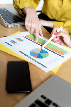 Close-up of two women working together on pie chart at desk in office