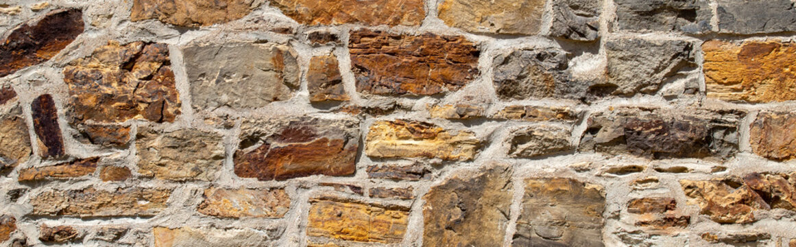 Old rustic multicolored stone wall background with weathered rough uneven blocks