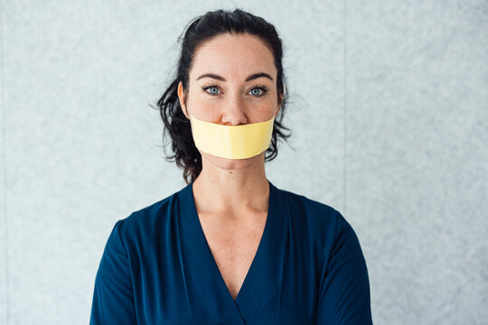 Woman with tape over mouth standing in front of gray wall