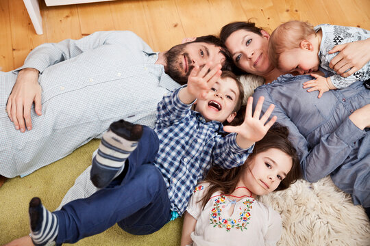 Family with three children lying on the floor at home looking at camera