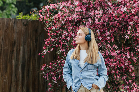 A blonde woman listens to music with headphones outdoors in spring