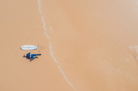 Portugal, Algarve, Sagres, Praia da Mareta, aerial view of man lying next to surfboard on the beach