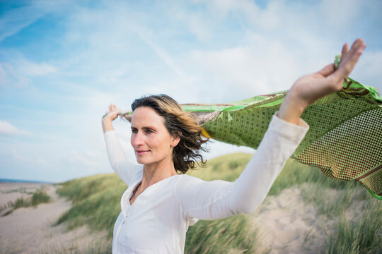Mature woman holding flapping scarf in the wind, relxiang in the dunes