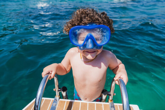 Smiling child with snorkeling mask climbing boat ladder in the ocean