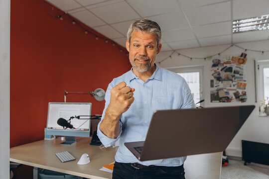 Excited businessman celebrates success with laptop in the office