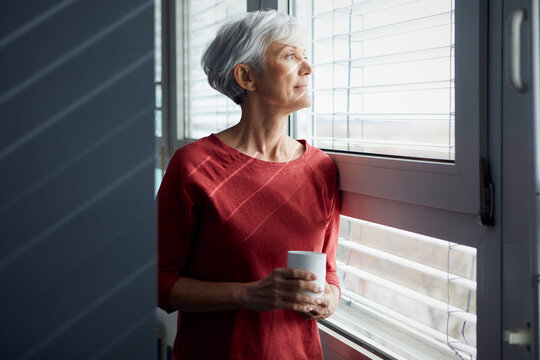 Portrait of senior woman with coffee mug looking out of window