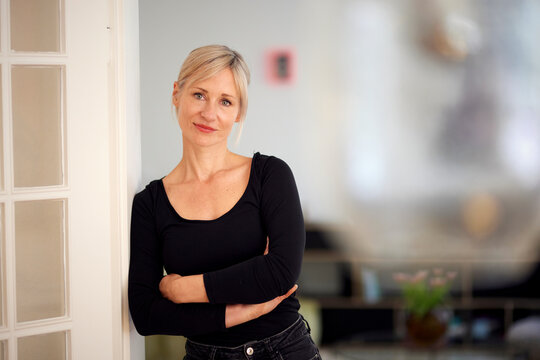 Smiling mature woman leans against a white door at home