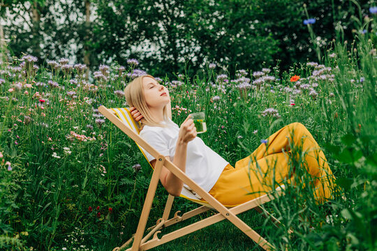 Woman relaxing in wildflower garden drinking tea during summer