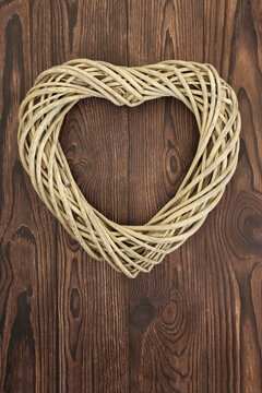 Heart shape wreath of woven wicker on rustic wood background. Natural romantic love garland frame symbol for home decor and valentines day. 