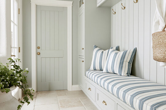 Modern Coastal mudroom featuring a built-in cushioned bench with blue-and-white stripes, dusty sage walls, and a paneled door in a bright setting