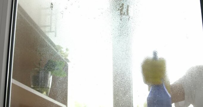 Window cleaning at home, cleaning solution sprayed onto the glass and wiped with a window squeegee.